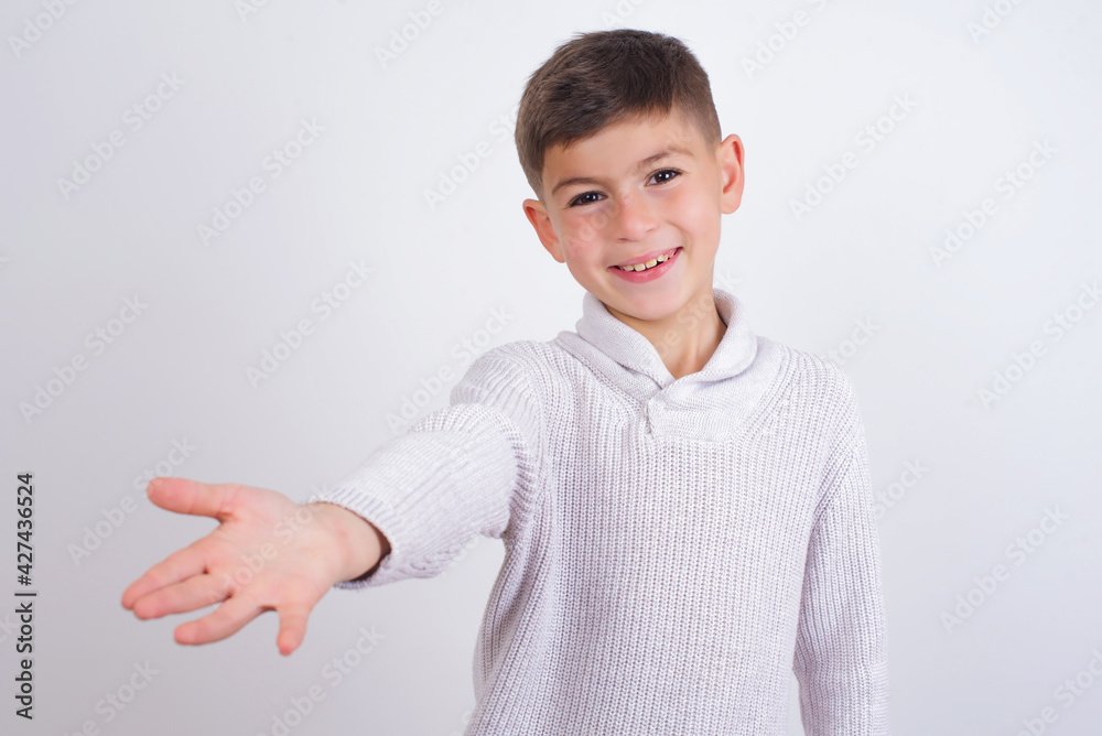 Caucasian kid boy wearing knitted sweater against white wall smiling friendly offering handshake as greeting and welcoming. Successful business. Caucasian kid boy wearing knitted sweater against white wall smiling friendly offering handshake as greeting and welcoming. Successful business.