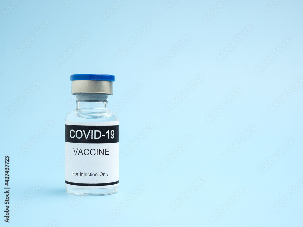 COVID-19 vaccine in a glass bottle placed on a light blue background. Vaccine for immunization, and treatment from coronavirus infection. Side view. Close-up photo. Concept of medical and healthcare COVID-19 vaccine in a glass bottle placed on a light blue background. Vaccine for immunization, and treatment from coronavirus infection. Side view. Close-up photo. Concept of medical and healthcare