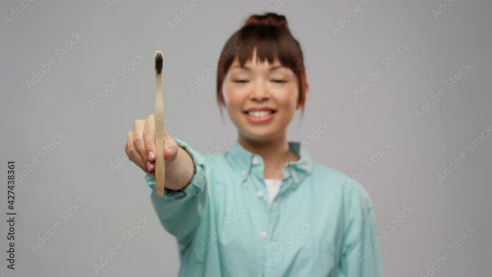 dental care, oral hygiene and people concept - portrait of happy smiling young asian woman in turquoise shirt with wooden toothbrush over grey background dental care, oral hygiene and people concept - portrait of happy smiling young asian woman in turquoise shirt with wooden toothbrush over grey background