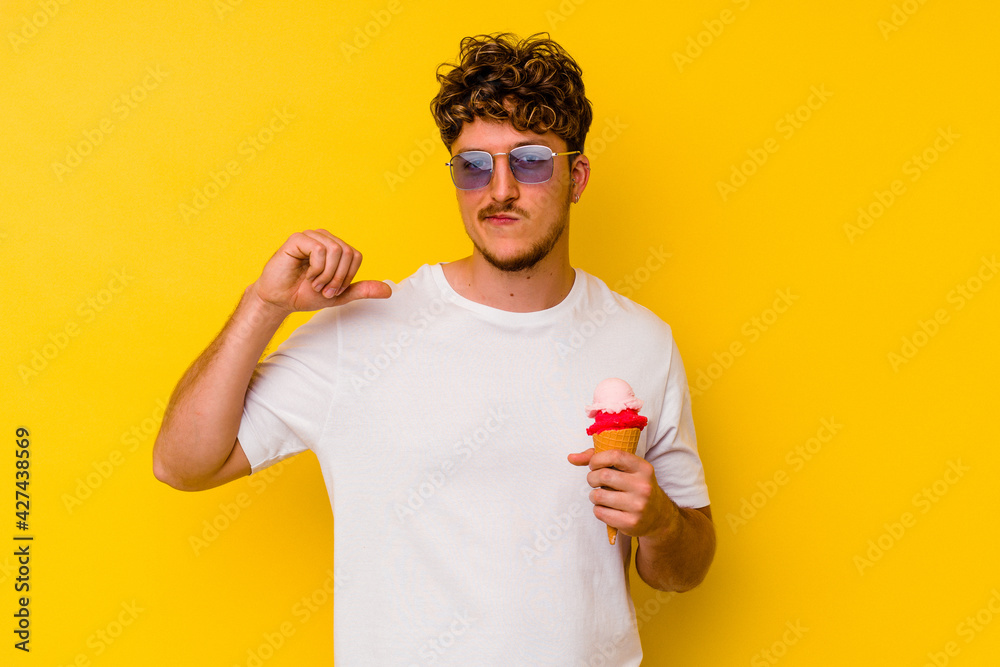 Young caucasian man eating an ice cream isolated on yellow background feels proud and self confident, example to follow. Young caucasian man eating an ice cream isolated on yellow background feels proud and self confident, example to follow.