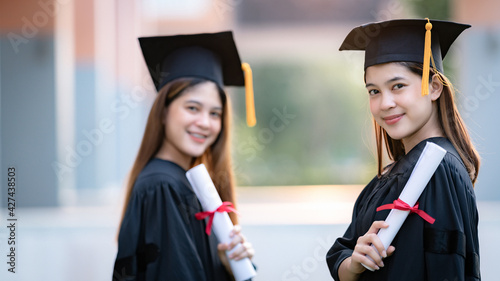 Young happy Asian woman university graduates in graduation gown and mortarboard hold a degree certificate celebrate education achievement in the university campus. Education stock photo