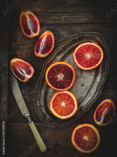 Sliced blood oranges on a vintage saucer and knife, dark mood, flat lay style