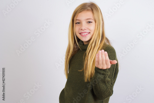 Caucasian kid girl wearing green knitted sweater against white wall inviting to come with hand. Happy that you came