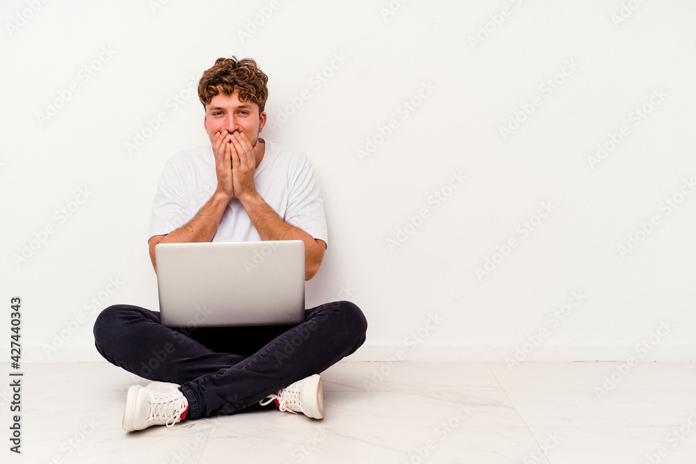 Young caucasian man sitting on the floor holding on laptop isolated on white background laughing about something, covering mouth with hands. Young caucasian man sitting on the floor holding on laptop isolated on white background laughing about something, covering mouth with hands.