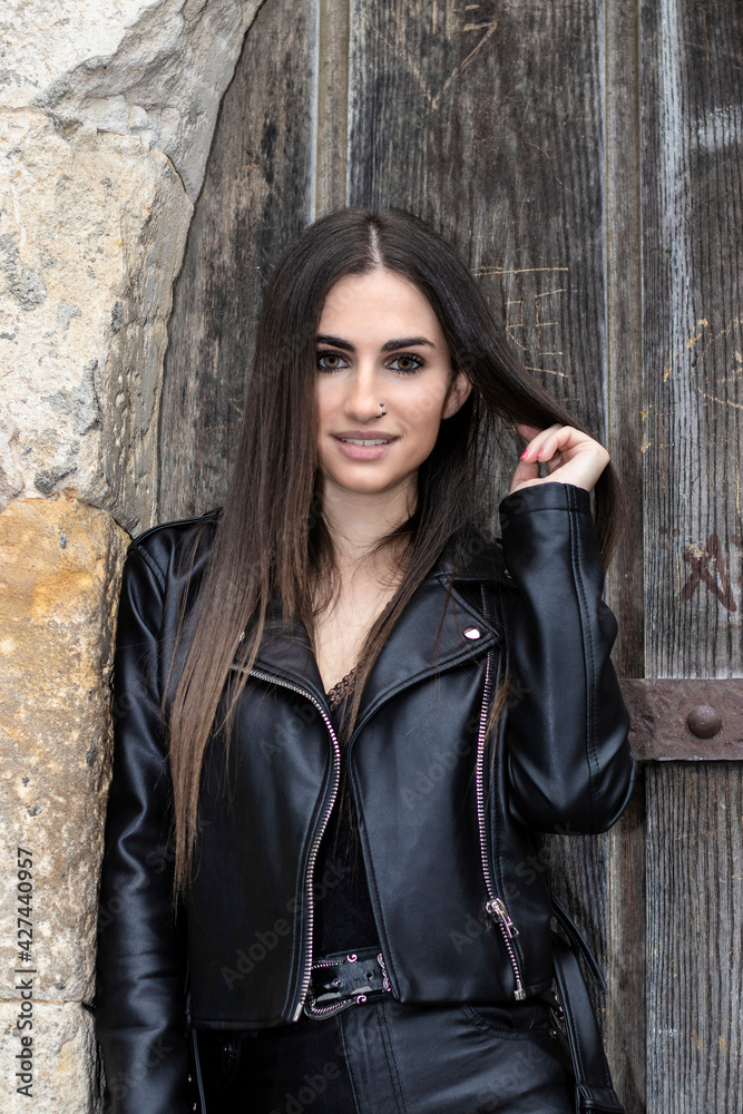 Fototapeta premium portrait of pretty young brunette woman dressed in a leather jacket in front of an old door