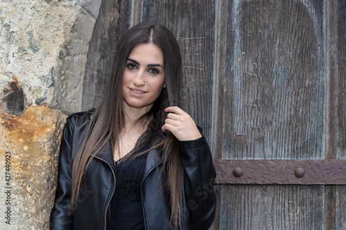 portrait of pretty young brunette woman dressed in a leather jacket in front of an old door © larrui
