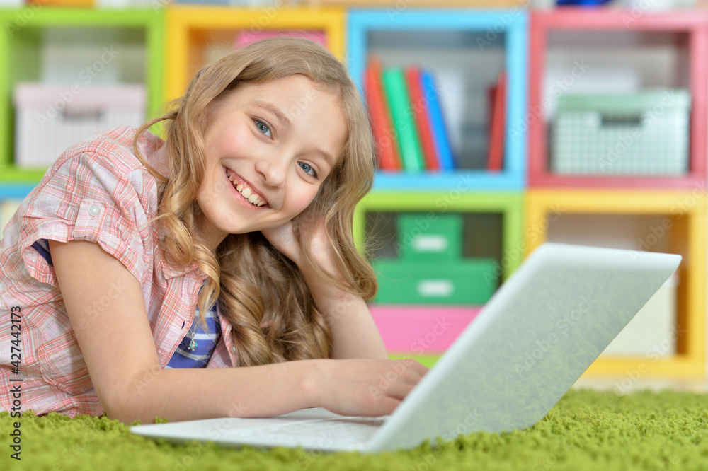 Cute girl using laptop while lying on green floor at home