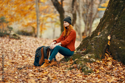 woman sitting near a tree in autumn forest and falling leaves landscape park