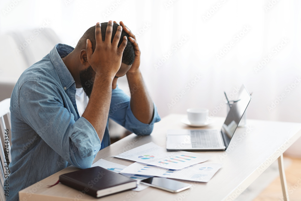 Stressed Black Entrepreneur Sitting At Desk And Looking At Financial Papers Stressed Black Entrepreneur Sitting At Desk And Looking At Financial Papers