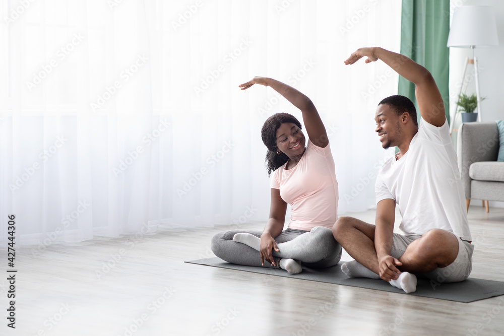 Positive african american couple sitting on fitness mat, stretching Positive african american couple sitting on fitness mat, stretching