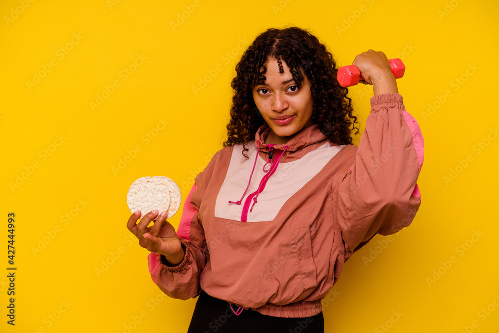 Young mixed race sport woman eating a rice cakes isolated on yellow background Young mixed race sport woman eating a rice cakes isolated on yellow background