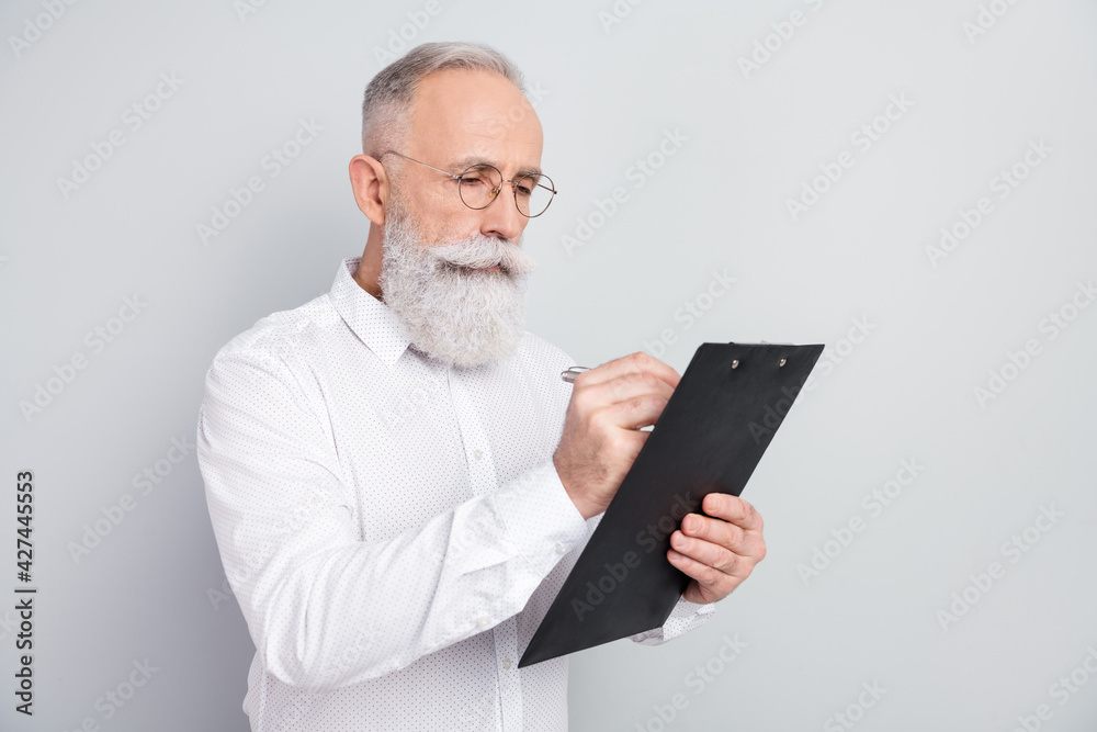 Photo of minded focused serious old man look write clipboard plan businessman isolated on grey color background Photo of minded focused serious old man look write clipboard plan businessman isolated on grey color background