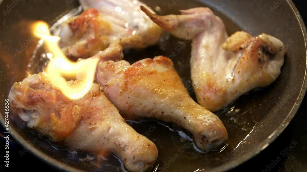 Close-up of chicken legs and wings fried in a pan in slow motion. Chicken legs and wings in spices are fried in a pan. Flashes of open fire in slow motion