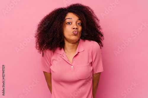 Young african american woman isolated on pink background shrugs shoulders and open eyes confused.