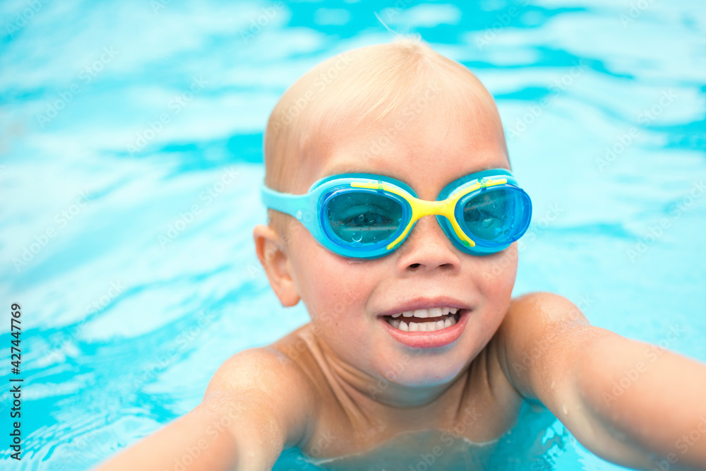 Little swimmer with swimming glasses in the swimming pool. Child, sport and activity concept.