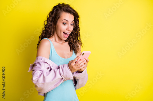 Portrait of attractive cheerful amazed wavy-haired girl using gadget having fun copy space isolated over bright yellow color background