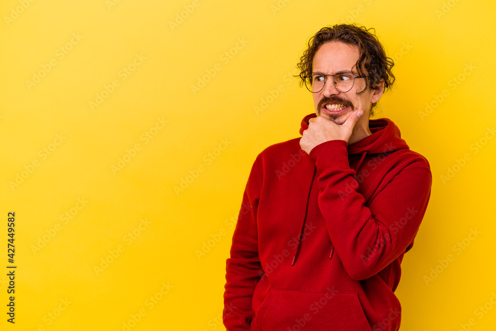 Young caucasian man isolated on yellow background touching back of head, thinking and making a choice.