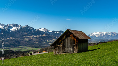 Eine alte Holzscheune, Heuschober oder Stadel in Düns, im Grossen Walsertal, mit Blick zum Rhätikon, Alpstein und Säntis. blauer Himmel und verschneite Bergspitzen.