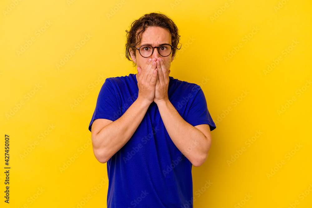 Young caucasian man isolated on yellow background covering mouth with hands looking worried. Young caucasian man isolated on yellow background covering mouth with hands looking worried.