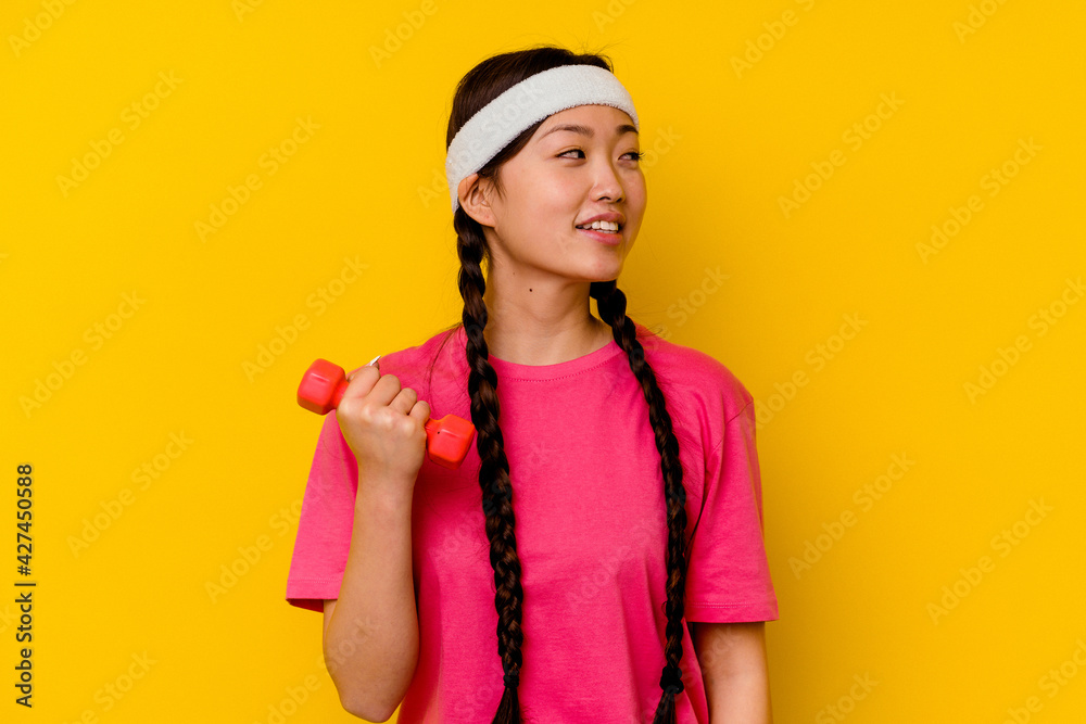 Young sport chinese woman isolated on yellow background looks aside smiling, cheerful and pleasant. Young sport chinese woman isolated on yellow background looks aside smiling, cheerful and pleasant.