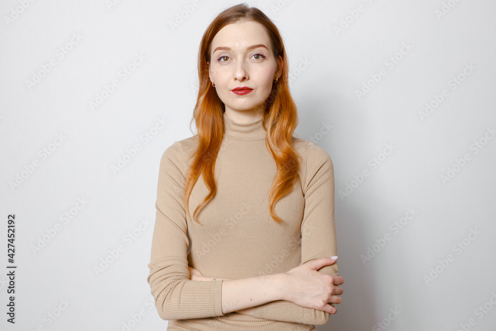 Portrait of a serious red-haired girl in a beige jacket. White background Portrait of a serious red-haired girl in a beige jacket. White background
