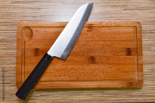 Cutting board and a kitchen knife on wooden background. Top view