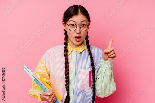 Young chinese student woman holding books wearing a fashion multicolour shirt and braid  isolated on pink background having some great idea  concept of creativity.
