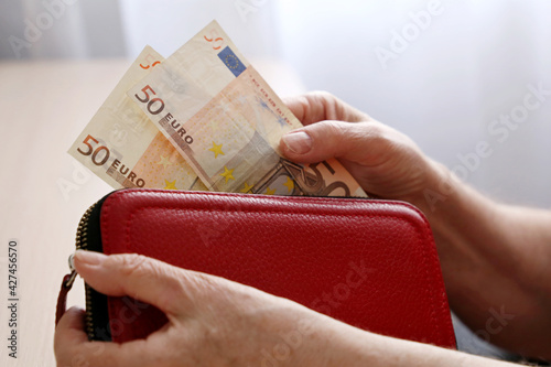 Elderly woman takes out a euro note from her wallet. Concept of pension payments, savings at retirement, pensioner with money