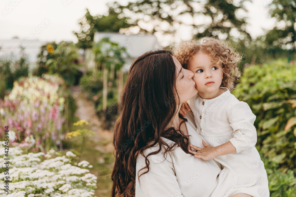 pretty curly daughter walking with her mother and posing for a photo in nature on flower alleys pretty curly daughter walking with her mother and posing for a photo in nature on flower alleys