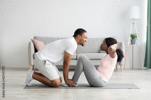 Athletic black couple exercising together at home, working on abs