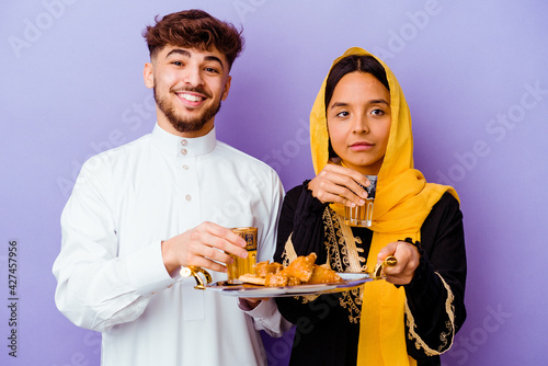 Young Moroccan couple drinking tea celebrating ramadan month isolated on purple background