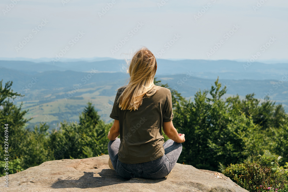 A woman is practicing meditation on a rock with a beautiful view of the mountains. Outdoor adventure. Healthy lifestyle, active rest. Tourism, travel and climbing concept. Enjoying the nature