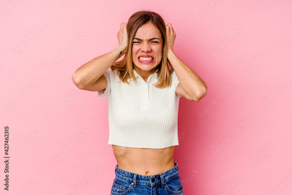Young caucasian woman isolated on pink background covering ears with hands trying not to hear too loud sound. Young caucasian woman isolated on pink background covering ears with hands trying not to hear too loud sound.
