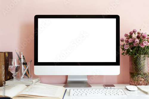Mock up of stylish accessories on desk at home office. Blank copy space screen of personal computer, textbook, glass of water and fresh bouquet on table. Student's workplace. Nobody around