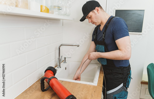 Plumber using drain snake to unclog kitchen sink.