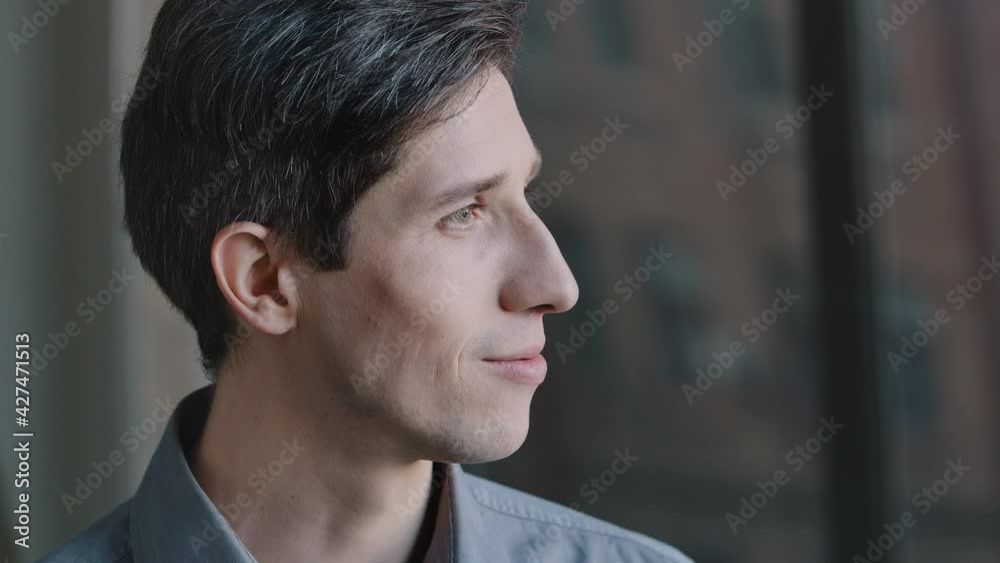 Close-up profile of thoughtful male face. Portrait of 30s caucasian businessman in office standing by window with pensive look thinking business strategy dreaming turning to camera looking smiling Close-up profile of thoughtful male face. Portrait of 30s caucasian businessman in office standing by window with pensive look thinking business strategy dreaming turning to camera looking smiling