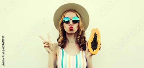Summer portrait of beautiful young woman posing with papaya wearing a straw hat, sunglasses on a white background