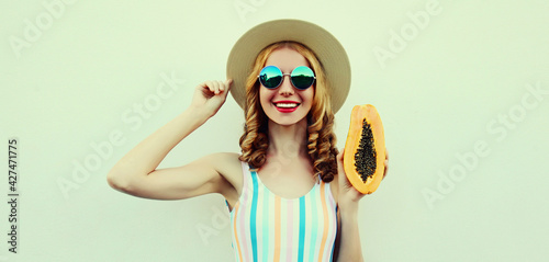 Summer portrait of happy smiling young woman with papaya wearing a straw hat, sunglasses on a white background