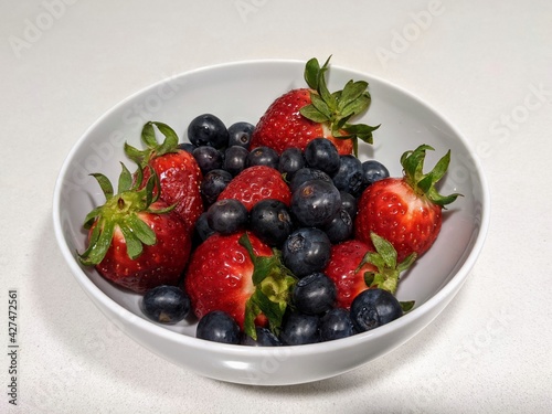 White bowl of strawberries and blueberries on a white colored table