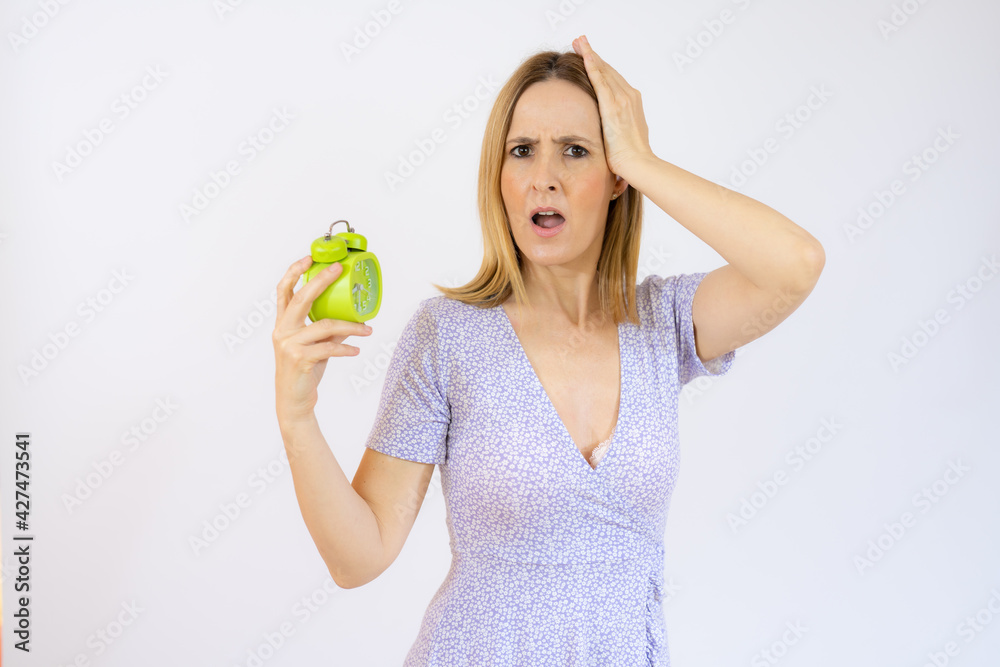 Young beautiful woman holding alarm clock standing over isolated white background with doubtful gesture Young beautiful woman holding alarm clock standing over isolated white background with doubtful gesture