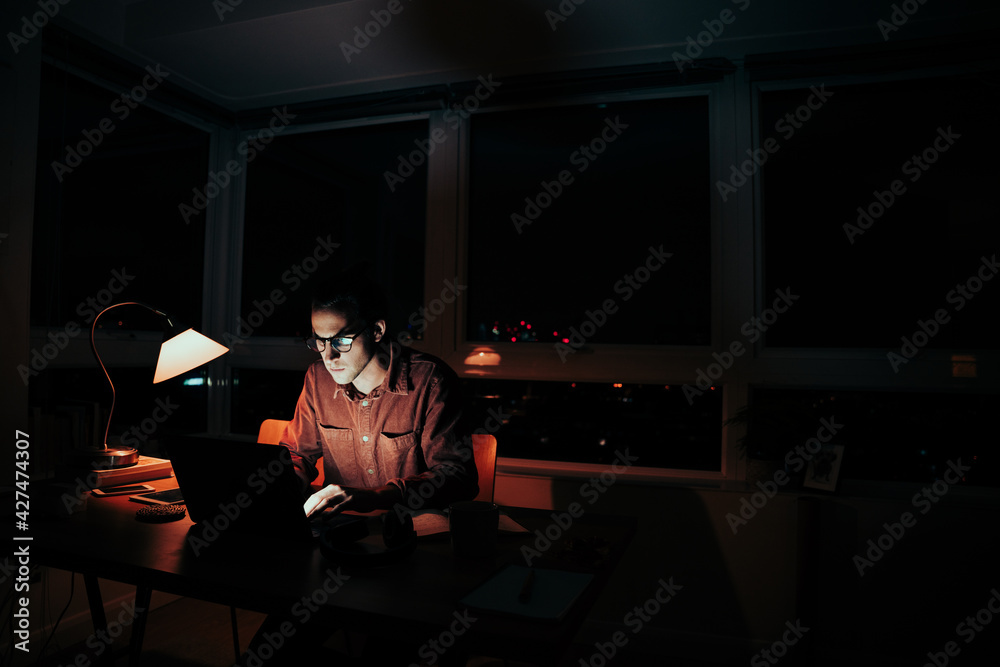 Caucasian male freelancer photographer sorting through images on laptop sitting at desk