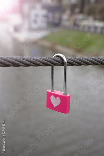 Little pink lock on wire rope. Love lock on the bridge.