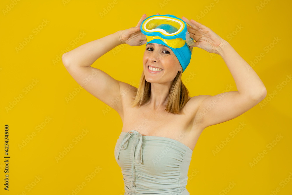 Smiling young woman wearing swimsuit and diving goggles isolated over yellow background Smiling young woman wearing swimsuit and diving goggles isolated over yellow background