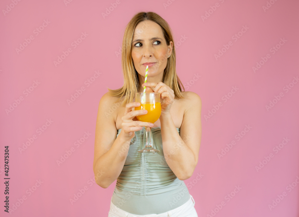 Young smiling woman drinking orange juice isolated over pink background Young smiling woman drinking orange juice isolated over pink background