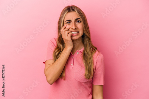 Young blonde caucasian woman isolated on pink background biting fingernails, nervous and very anxious.