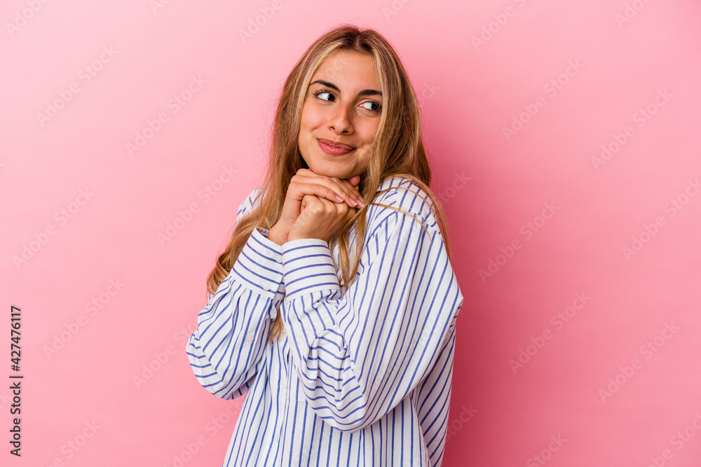 Young blonde caucasian woman isolated on pink background keeps hands under chin, is looking happily aside. Young blonde caucasian woman isolated on pink background keeps hands under chin, is looking happily aside.