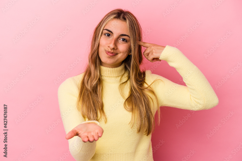Young blonde caucasian woman isolated on pink background holding and showing a product on hand. Young blonde caucasian woman isolated on pink background holding and showing a product on hand.