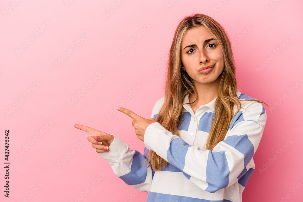 Young blonde caucasian woman isolated on pink background shocked pointing with index fingers to a copy space. Young blonde caucasian woman isolated on pink background shocked pointing with index fingers to a copy space.