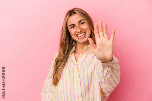 Young blonde caucasian woman isolated on pink background smiling cheerful showing number five with fingers.