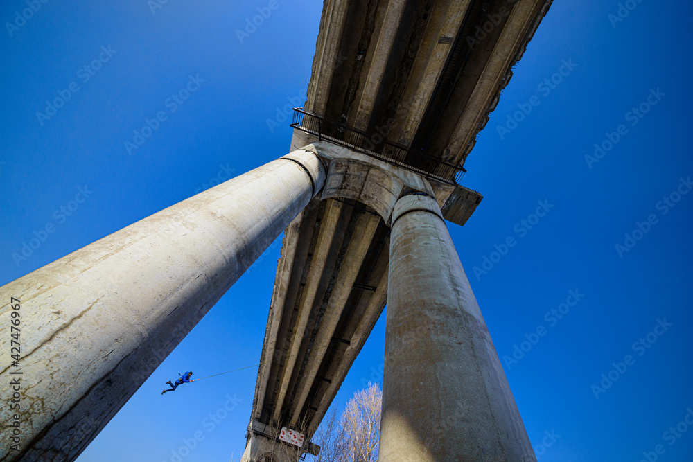Fototapeta premium bottom view of man jumping from high bridge on sky background at sunny day 